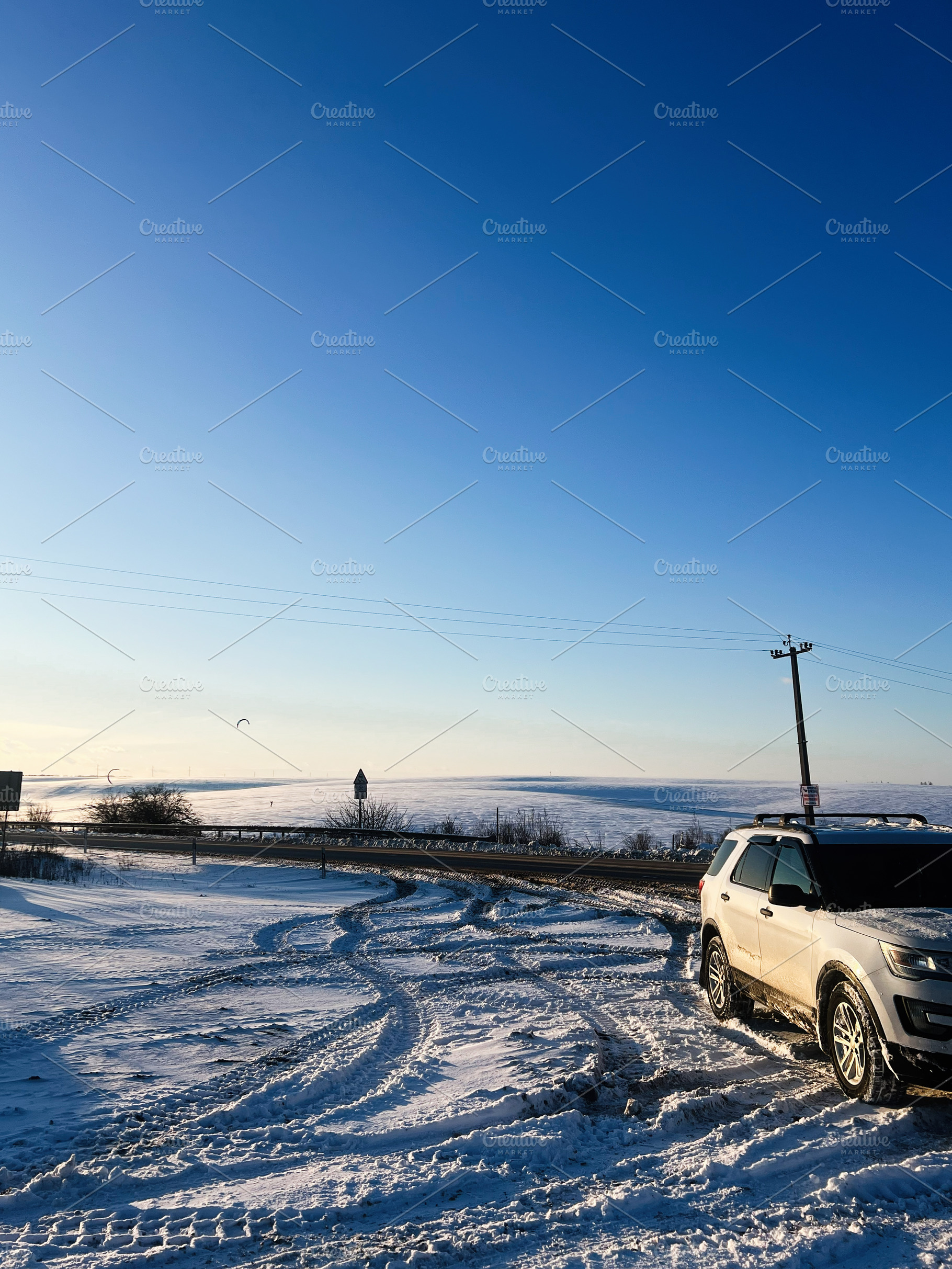 Snowy roadside scene with SUV parked on a snow covered road under a clear blue, a Photo by AS photostudio