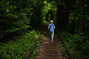 Boy walking along a scenic railway path surrounded by lush green foliage, a Photo by AS photostudio