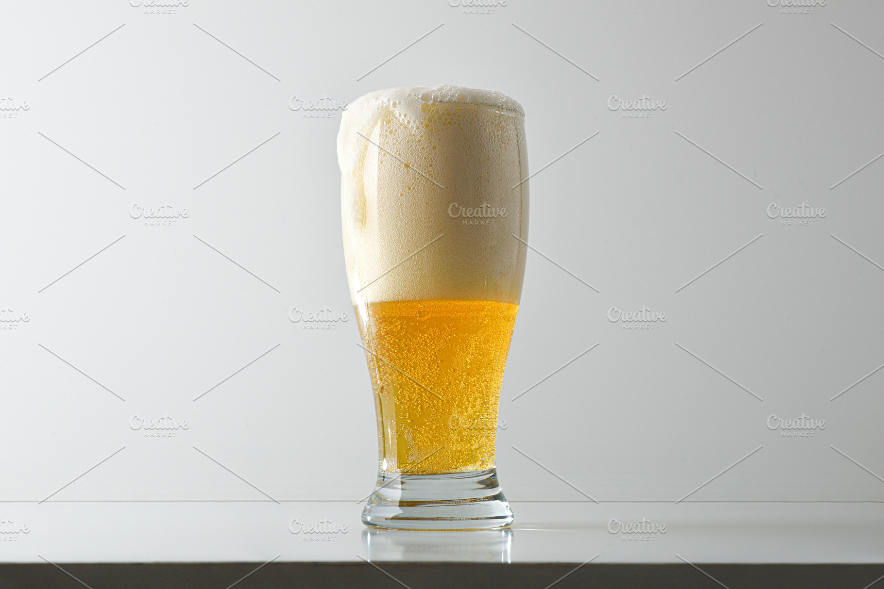 Glass of foamy beer on table and white isolated background, a Food & Drink Photo by Davizro's Market