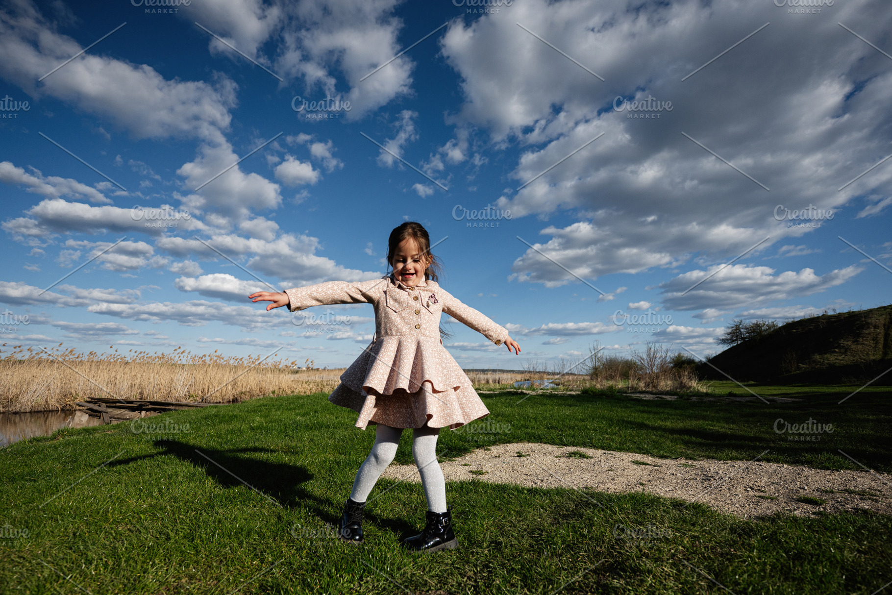 Young girl spinning and playing outdoors in a pink dress under dramatic blue sk, a Person Photo by AS photostudio