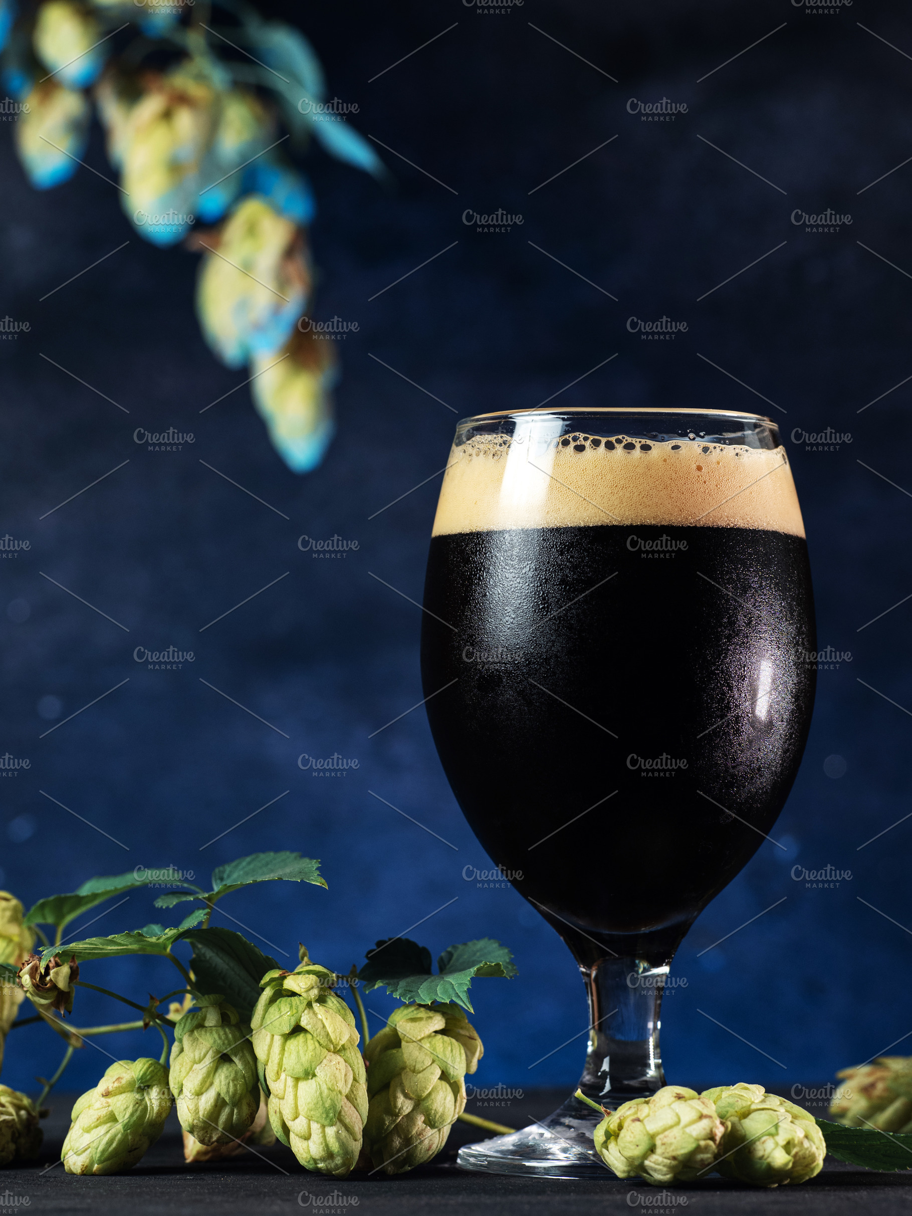 Glass of beer stout on a dark blue background, green hops, a Food & Drink Photo by PavelKant