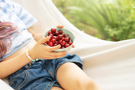 A little girl rests in a hammock and eats cherries in the summer, a Sports & Recreation Photo by Olena Rudo
