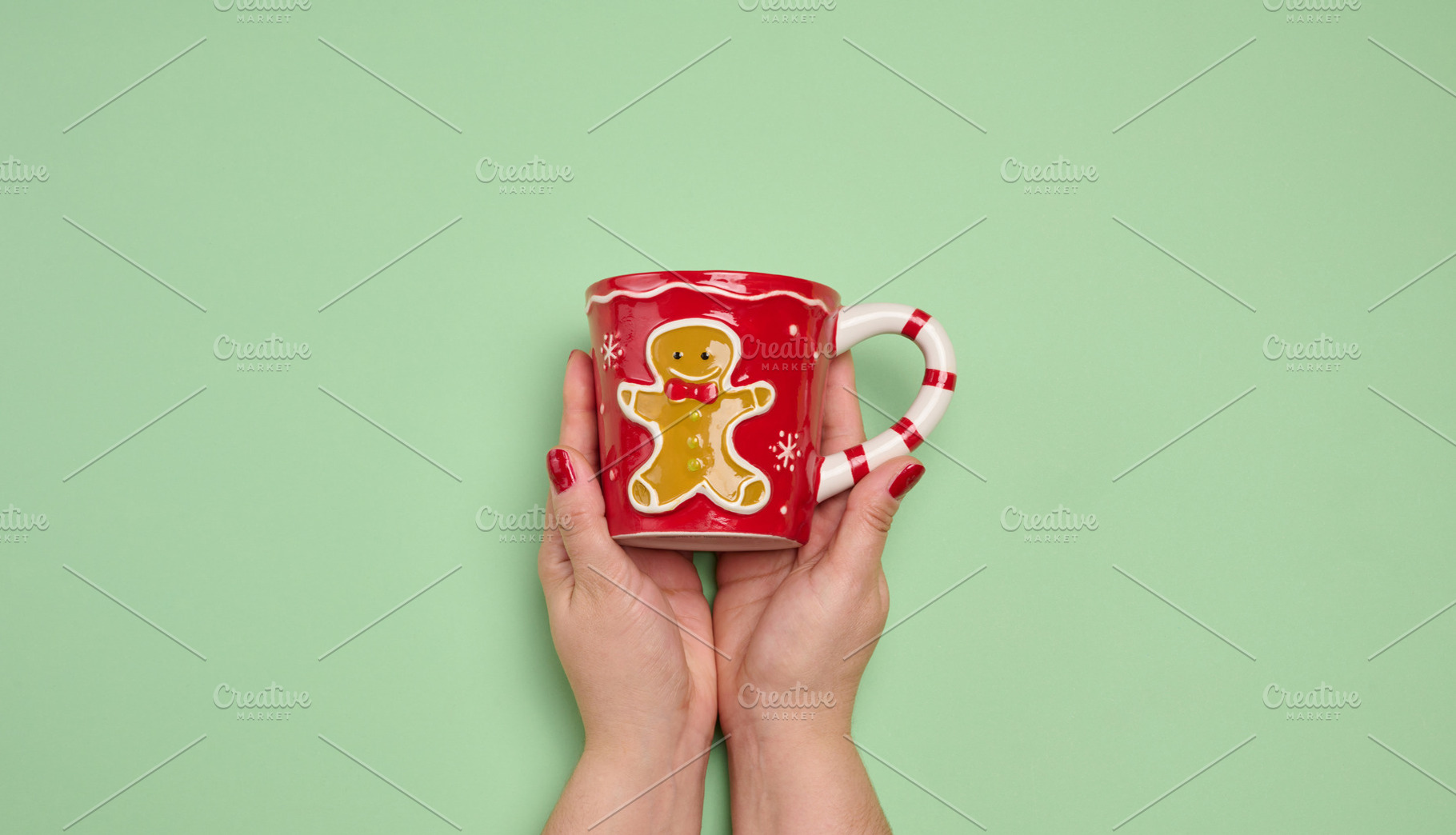 Two female hands holding a red Christmas mug with a gingerbread, a Holiday Photo by ndanko