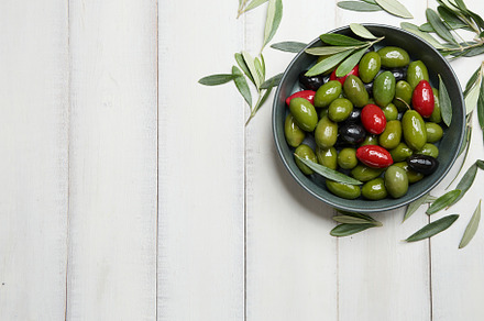 Mixed green, black and red olives in big bowl on white planks background