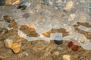 Water flowing over smooth stones creates mesmerizing patterns at a riverbed, a Photo by AlyaAnd
