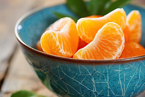Fresh mandarin wedges in a bowl with green leaves on a rustic wooden table, a Food & Drink Photo by AlyaAnd