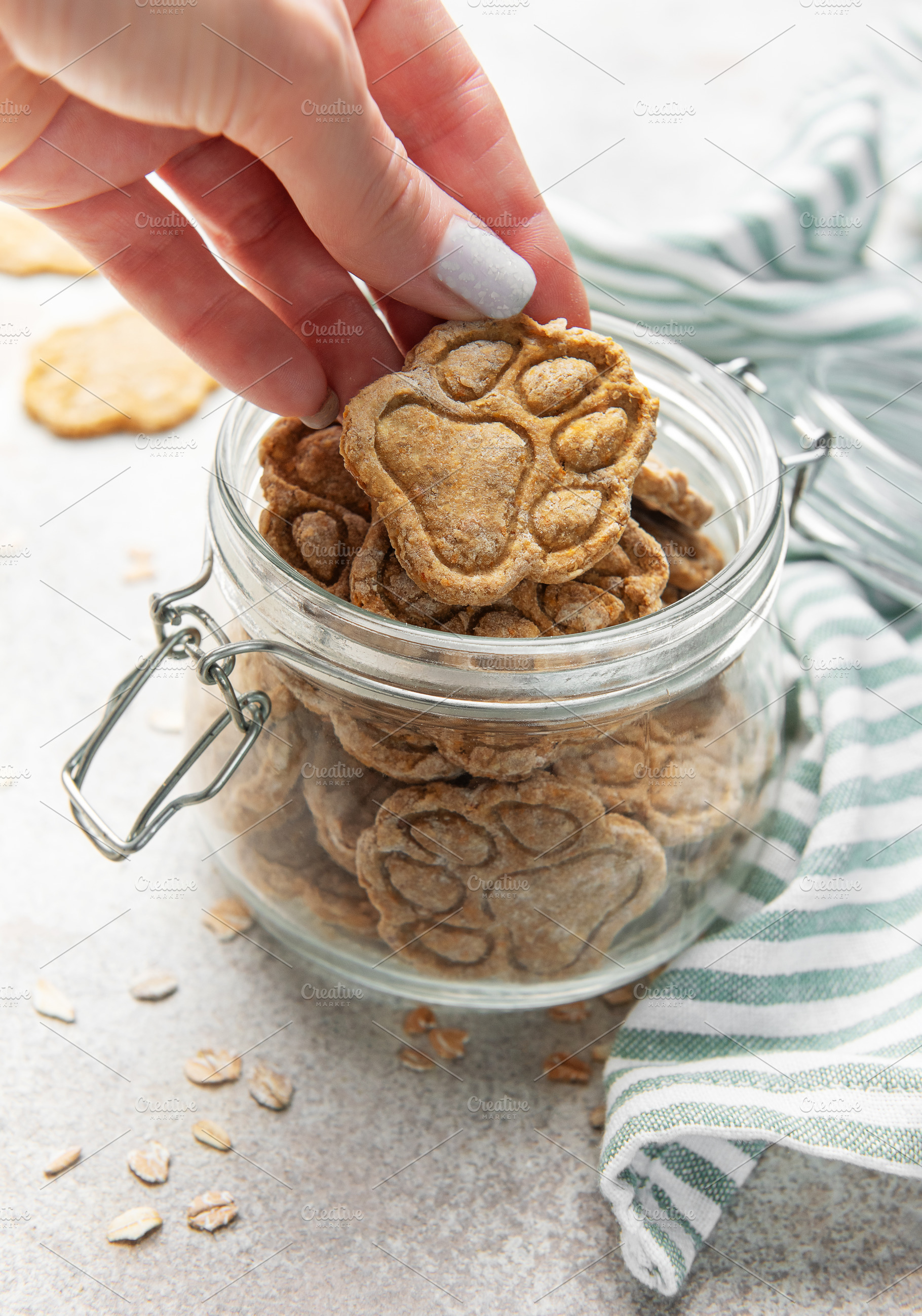 Woman hand taking homemade paw print dog treats from jar, a Food & Drink Photo by Olena Rudo