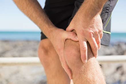 Fit man gripping his injured knee, a Photo by wavebreak
