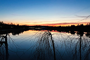 Serene twilight pond reflecting vibrant sunset colors with silhouettes of trees, a Photo by AS photostudio