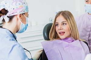 Dentist wearing surgical mask listening to young woman in dental clinic, a Health & Medical Photo by Antonio Gravante Market