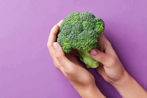 Hand holding fresh broccoli on purple background, a Food & Drink Photo by AlyaAnd