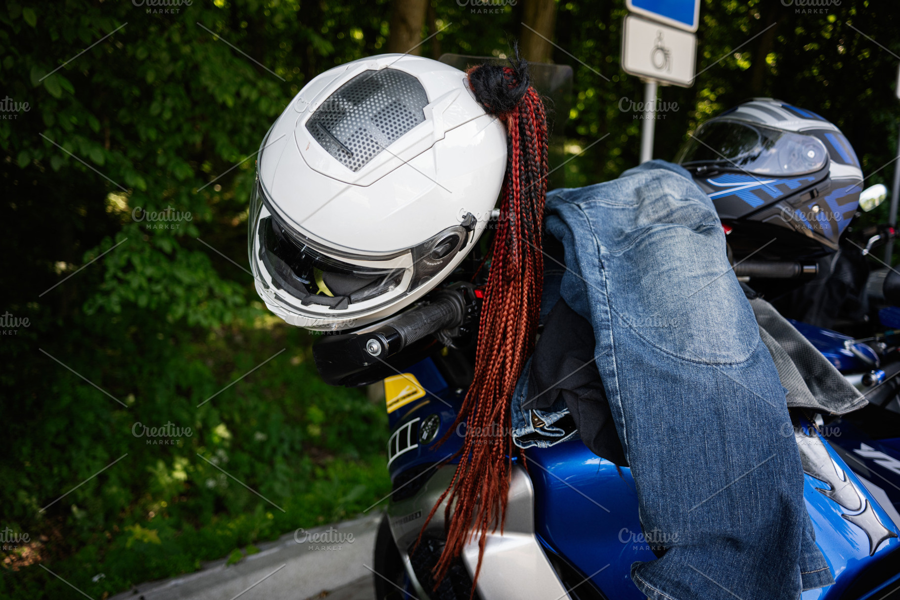 Motorcycle helmet and clothing on a parked bike near a wooded roadside, a Photo by AS photostudio