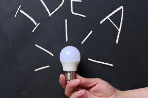 Hand holds a lit light bulb against a black chalkboard with the, a Business Photo by ndanko
