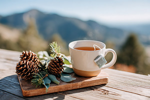 Warm tea served on rustic wooden tray with pinecones and greenery in scenic mou, a Food & Drink Photo by AlyaAnd