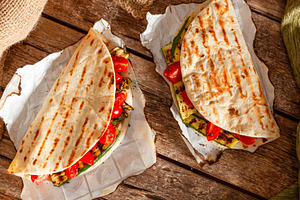 Two piadine with grilled zucchini and tomatoes resting on baking paper sheets, a Food & Drink Photo by Antonio Gravante Market