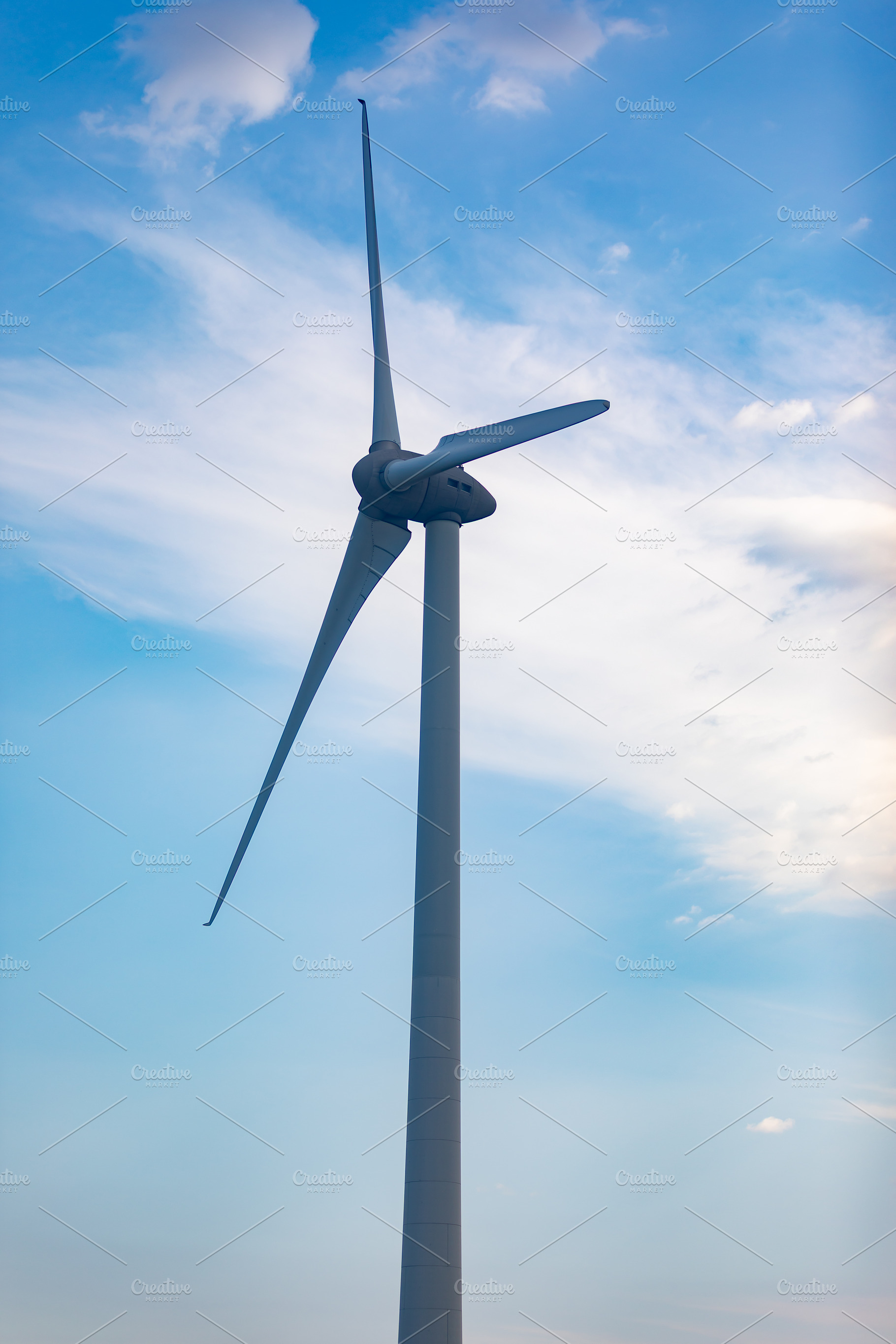 Close-up of a sleek wind turbine with rotating blades set against a bright blue, a Technology Photo by Ales Munt