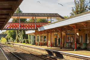Vintage train station platform and red footbridge with tracks and signals. Kemb, a Photo by Studio ANNA