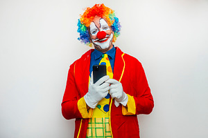 Clown holding smartphone with silly smile, a Person Photo by karrastock