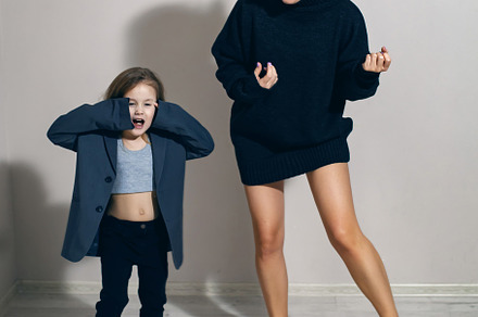 funny portrait of a fashionable girl child in a large gray jacket stands agains, a Person Photo by SaulichPhoto