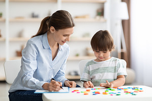 Cute little boy study to read with professional tutor, positive woman tutor hel, a Photo by Prostock-Studio