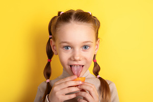 Cheerful young girl with braided hair tasting an orange slice ag, a Person Photo by Ales Munt