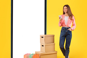 Lady Standing Near Cellphone, Shopping Bags And Boxes, Yellow Background, a Photo by Prostock-Studio