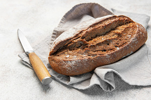 Rustic dark bread loaf with knife on napkin, a Food & Drink Photo by Olena Rudo