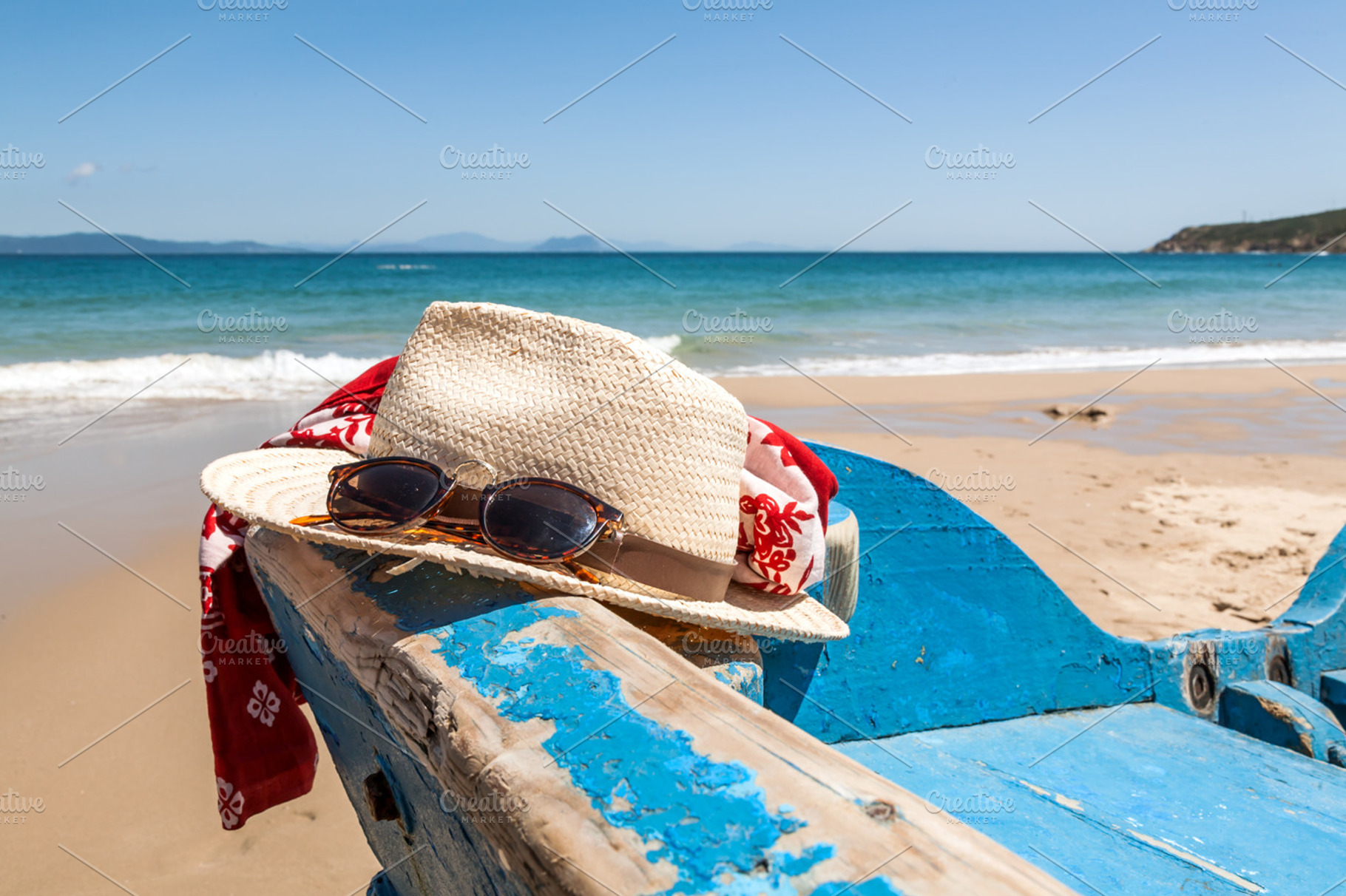 Travel things on the beach containing sunglasses, hat, and scarf