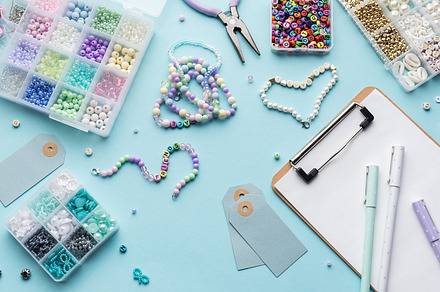 Colorful beads, pliers, clipboard and price tags arranged on blu, a Beauty & Fashion Photo by Olena Rudo