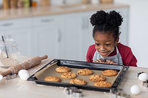 Emotional little black girl looking at fresh homemade cookies, a Photo by Prostock-Studio