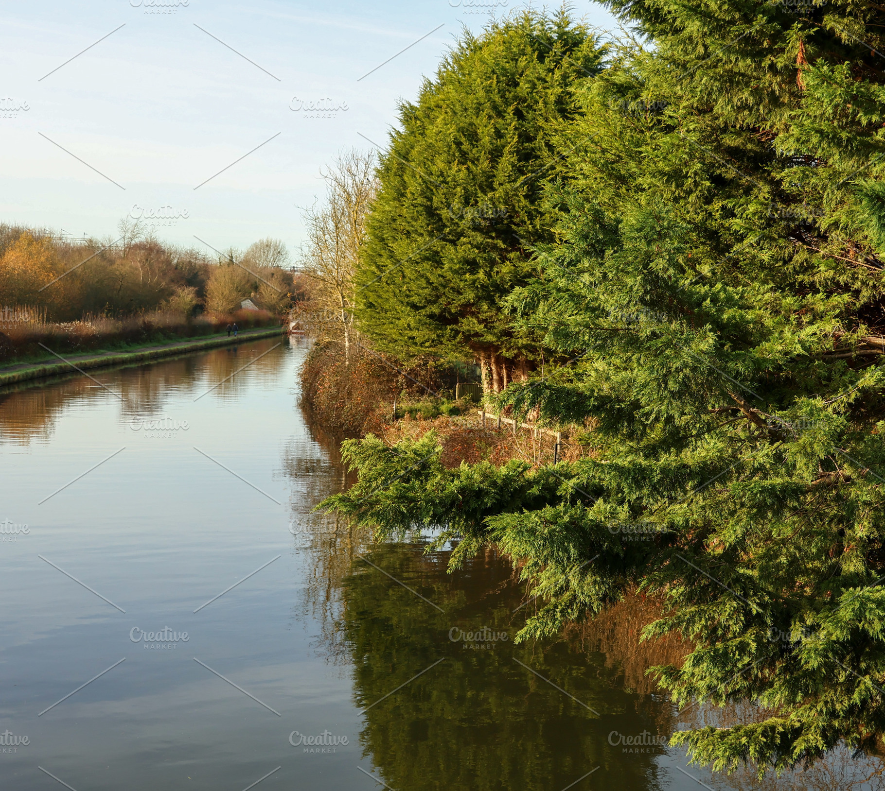 Canal scene reflecting green trees and clear blue sky on a calm morning, offeri, a Photo by Studio ANNA