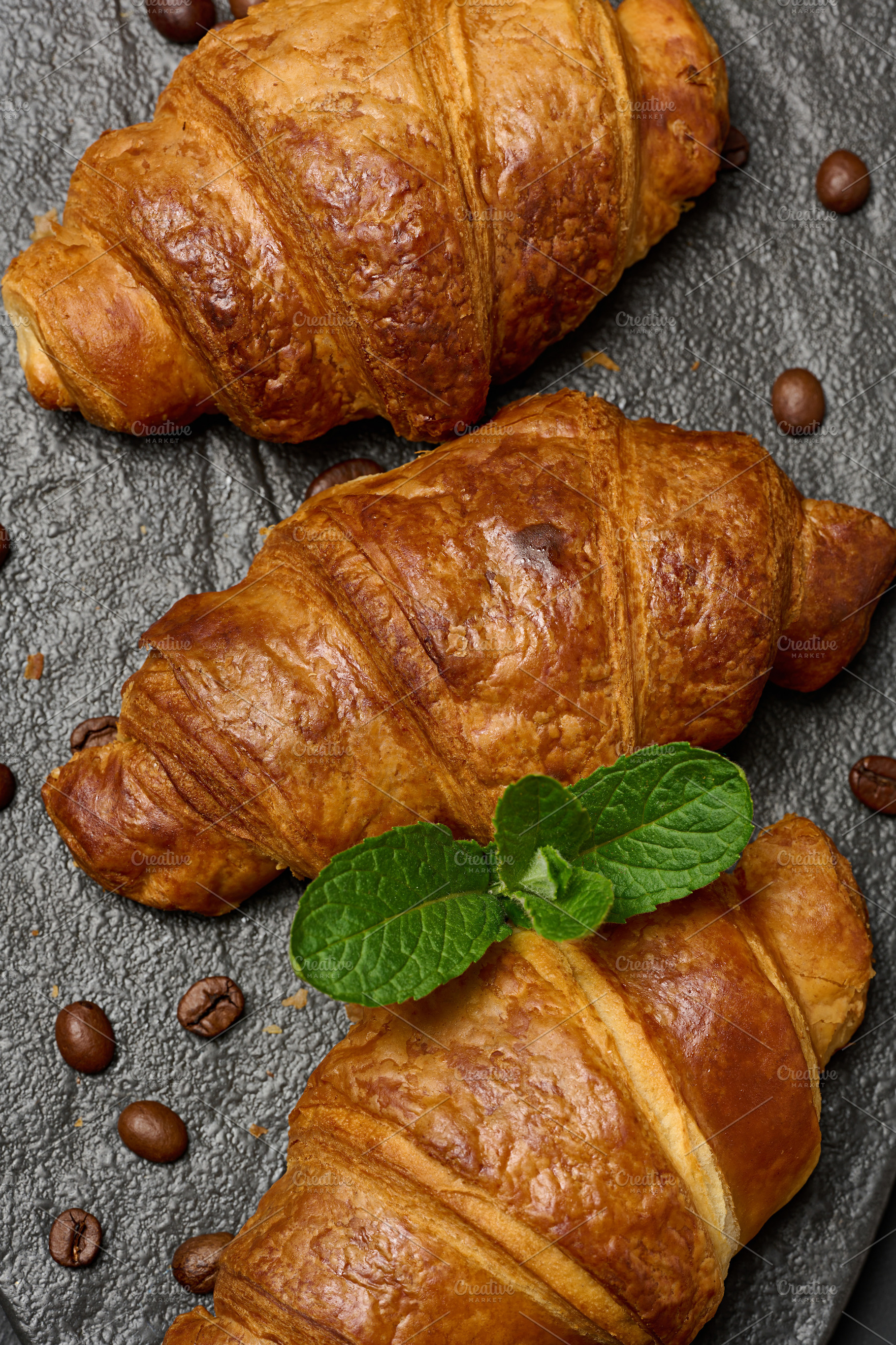 Golden croissants lined up on a dark stone board with a sprig of, a Food & Drink Photo by ndanko
