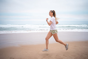 Happy sporty woman jogging on wet seashore against sky at beach, a Person Photo by andreonegin market
