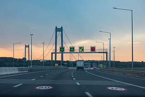 Empty highway leading to a large suspension bridge at dusk with illuminated lan, a Transportation Photo by Ales Munt