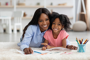 Portrait of cheerful loving mom and little girl coloring together, a Photo by Prostock-Studio