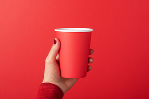 Female hand holding a red paper cup against a matching red backg, a Food & Drink Photo by Ales Munt