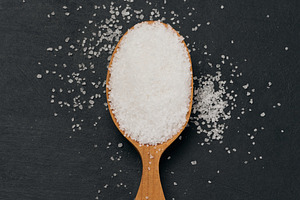 Handful of salt in a wooden spoon on a black table, top view, a Food & Drink Photo by ndanko