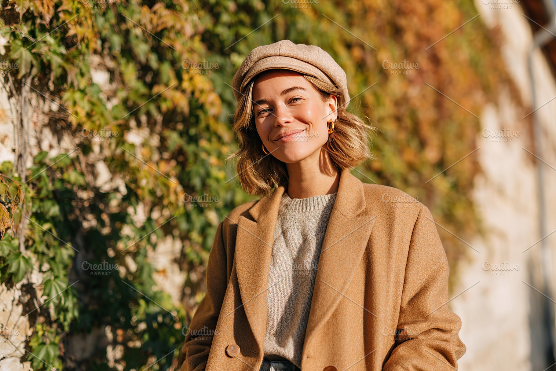 Young woman smiles warmly in a stylish outfit against a backdrop of ivy in autu, a Photo by AlyaAnd