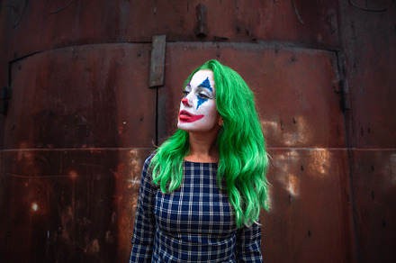 Portrait of a greenhaired girl in chekered dress with joker makeup on a rusty m