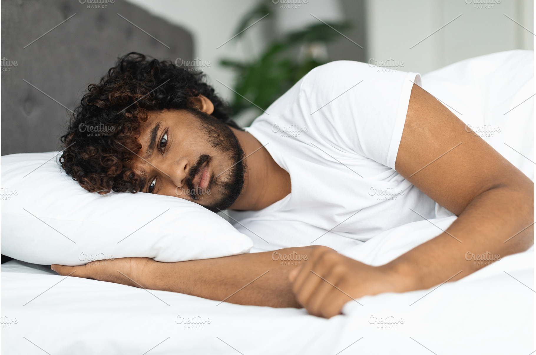Sad indian guy in pajamas laying in, a Person Photo by Prostock-Studio