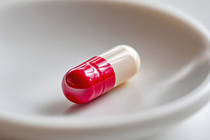 Close-up view of a single red and white capsule resting on a plate, a Photo by AlyaAnd