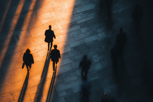 Silhouetted pedestrians walking in warm sunlight with long shadows on city pave, a Person Photo by AS photostudio