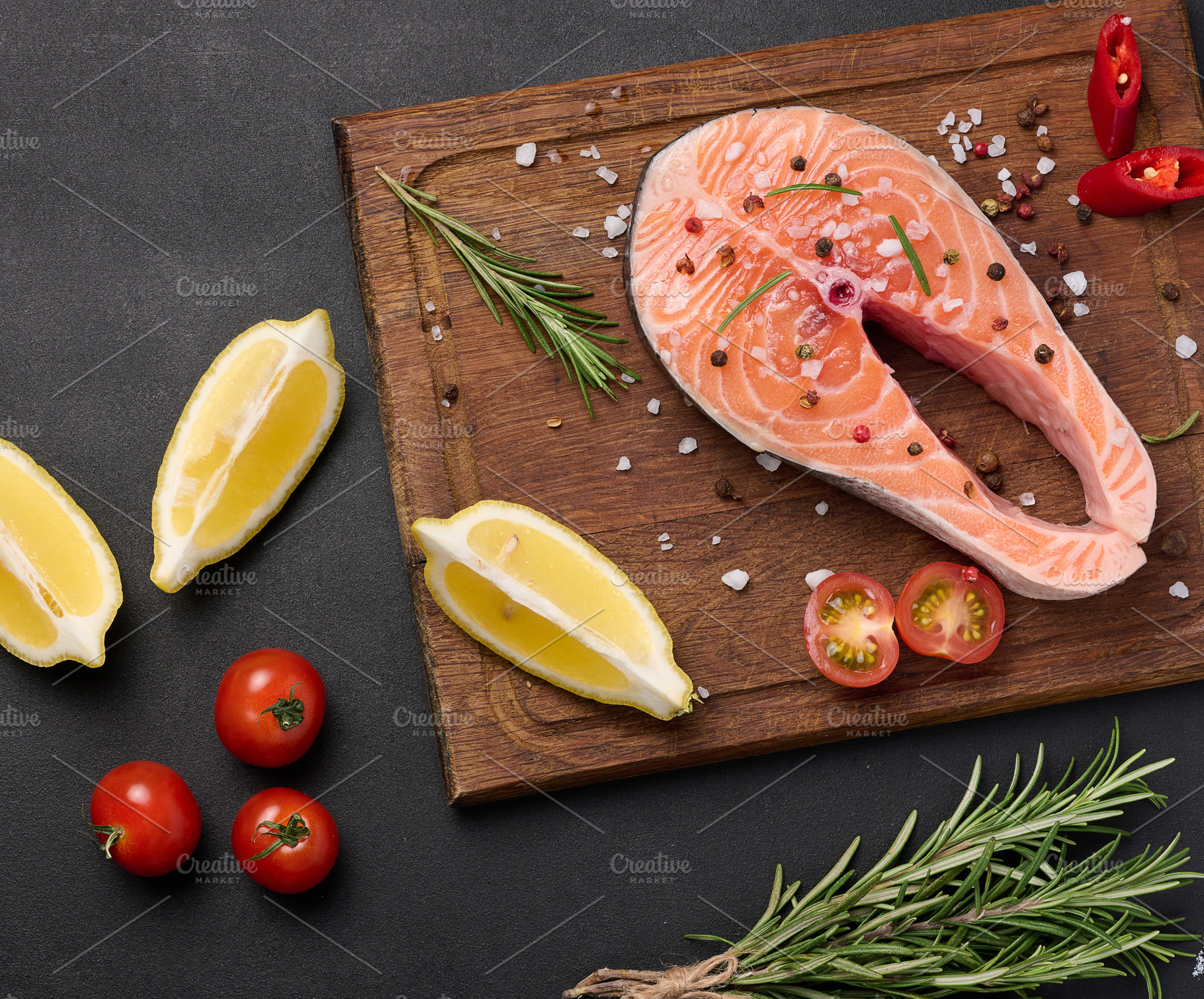 Raw salmon steak on a wooden cutting board, lemon slices, spices, a Food & Drink Photo by ndanko