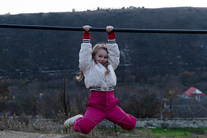 Smiling young girl in winter clothes hanging from a horizontal b, a Person Photo by Ales Munt