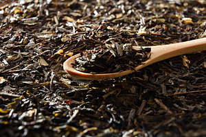 Wooden spoon filled with tea leaves on background of tea, a Food & Drink Photo by Davizro's Market