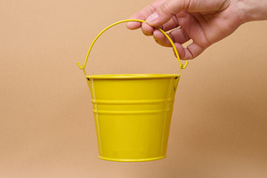 A person holding a small yellow bucket by the handle against a b, a Person Photo by ndanko