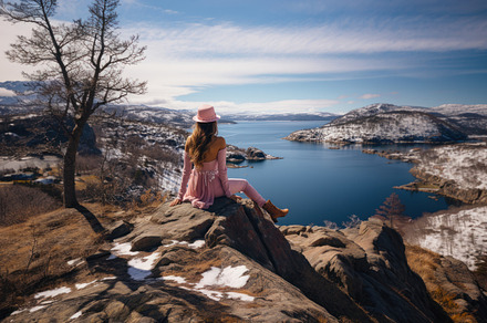 A young woman in a pink dress and hat sits on the edge of a clif, a Photo by AS photostudio