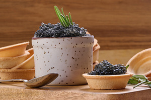 Black caviar in mini tartlet on wooden board, ceramic pot with c, a Food & Drink Photo by ndanko