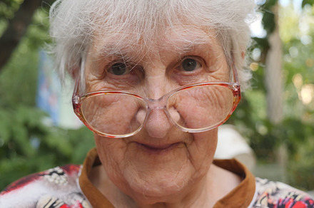 Old woman in eyeglasses looking into camera and smiling outdoor. Portrait of happy granny in glasses spending time outside. Emotions of grandmother. Close up Slow motion