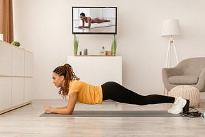Female Doing Plank Watching Sport Channel On TV At Home, a Photo by Prostock-Studio